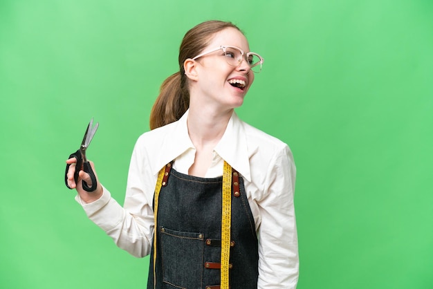 Seamstress woman over isolated chroma key background laughing in lateral position