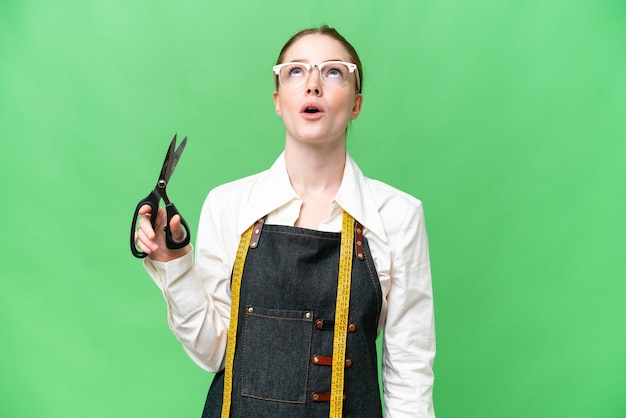 Seamstress woman over isolated chroma key background looking up and with surprised expression