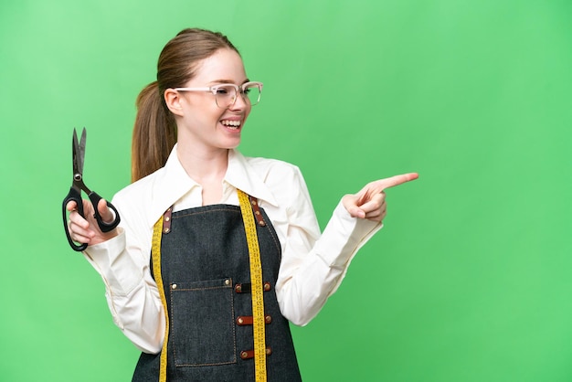 Seamstress woman over isolated chroma key background pointing finger to the side and presenting a product