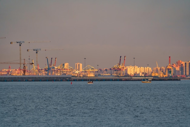 Seaport construction cranes and cranes of the cargo port on the sea horizon in sunset light