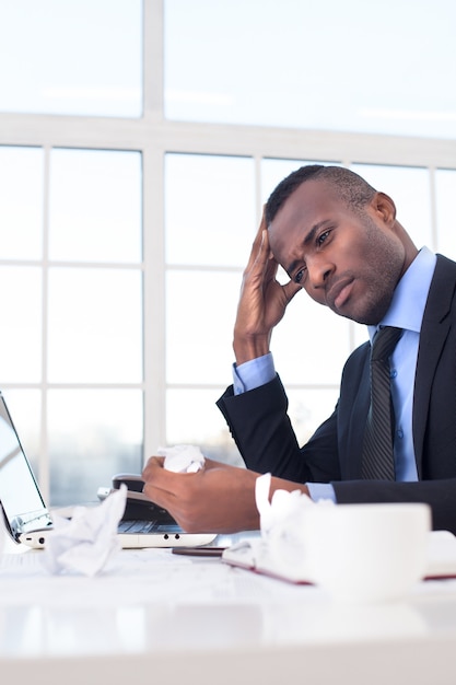 In search of the fresh ideas. Handsome young African businessman sitting at his working place and holding head in hand