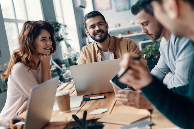 Searching for fresh ideas together. Group of young modern people in smart casual wear discussing something and smiling while working in the creative office