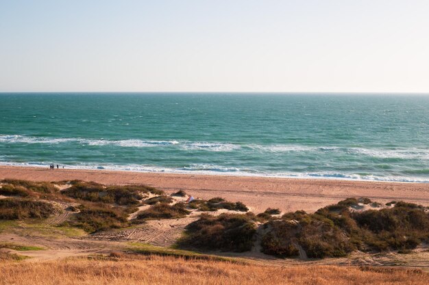 Seascape blue sea and sandy shore with dunes on an autumn day tourists walking in the background