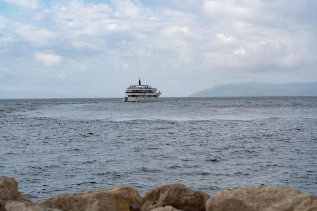 Seascape A large tourist liner floats on the waves to the island Mountains on the horizon In the foreground are large stones ship at sea