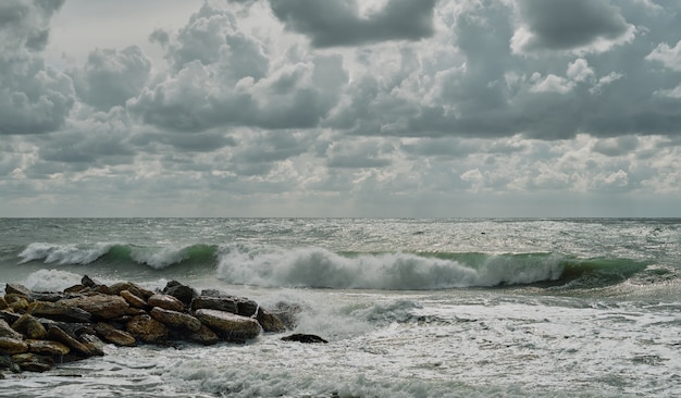 Seascape, waves break on the stone breakwater. Autumn storm on the coast, with waves in white foam, beautiful sky with clouds, sunny and windy day