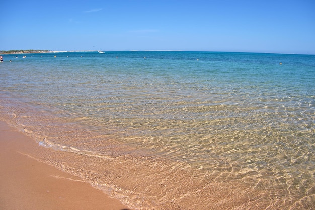 Seascape with surface of blue sea water with small ripple waves crashing on yellow sandy beach Travel and vacations concept