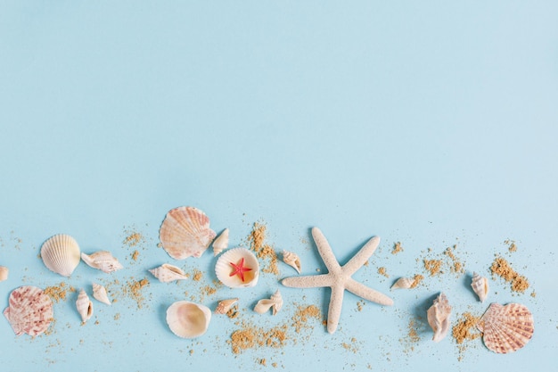 Seashells and beach sand on blue background top view Sea summer background with copy space space