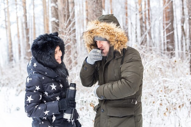 Season and walk concept - Happy couple drinking hot tea in winter forest