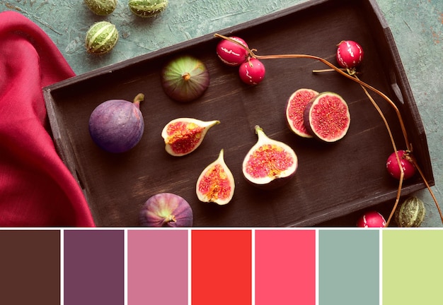 Seasonal Autumn Fall color matching palette Fresh halved fig fruits on black wooden tray Raspberry red silk scarf and deco fruits on turquoise board