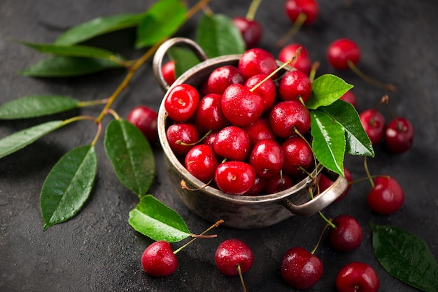 Seasonal harvesting of berries and fruits for the winter Cherry jam Cherry summer background A large number of cherries with leaves on the table in a saucepan on a black background closeup