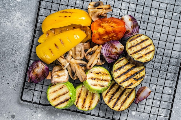 Seasonal summer Grilled vegetables on a grill bell pepper zucchini eggplant onion and tomato Gray background Top view