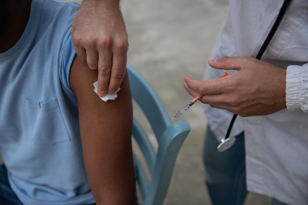 A seated patient has his shoulder been prepared for him to take his injection