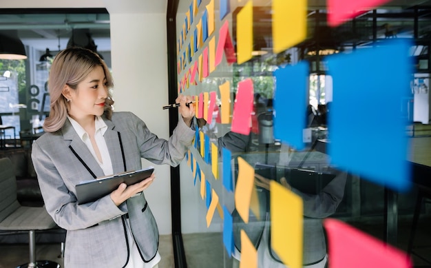 Secretary working in modern office in skyscraper writing and sticking adhesive notes with tasks on window modern officexA