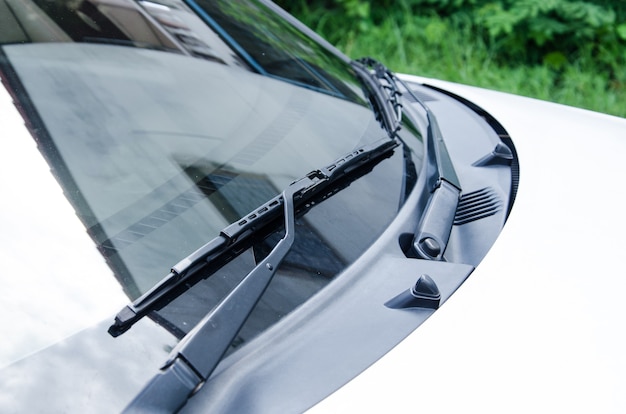 Section of the front of a white vehicle and its front windscreen bonnet and wipers.