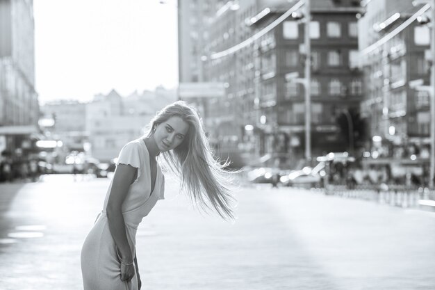 Photo seductive blonde woman with long hair wears dress walking at the city. black and white toning. space for text