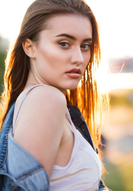 Seductive brunette young woman with perfect skin posing in rays of sun at sunset