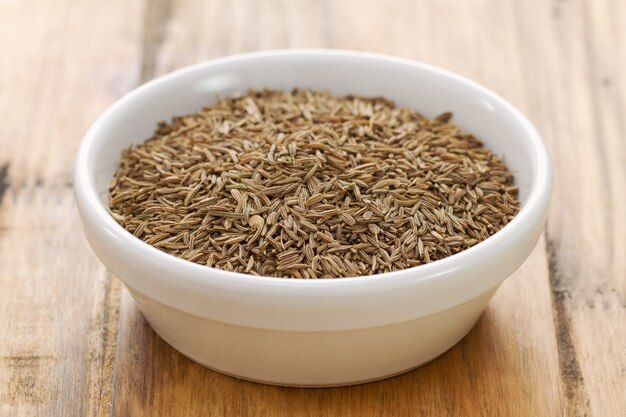 Seeds of carum in white bowl on brown wooden background