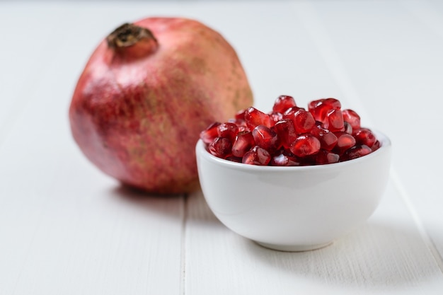 Seeds of ripe pomegranate in white Cup on white wooden table. Harvest ripe pomegranate