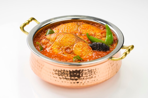 Seer Fish curry traditional Indian fish curry kerala special arranged in a copper serving bowl garnished with malabar tamarind and fresh green chilli on a white textured backgroundisolated