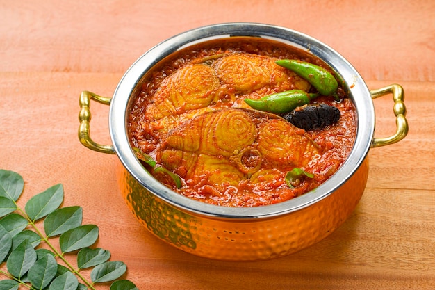 Seer Fish  or king fish curry kerala special dish arranged in a copper bowl garnished with curry leaves and fresh green chilli on a wooden textured backgroundisolated