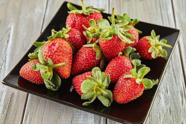 Selected fresh strawberries stacked on black plate on wooden background