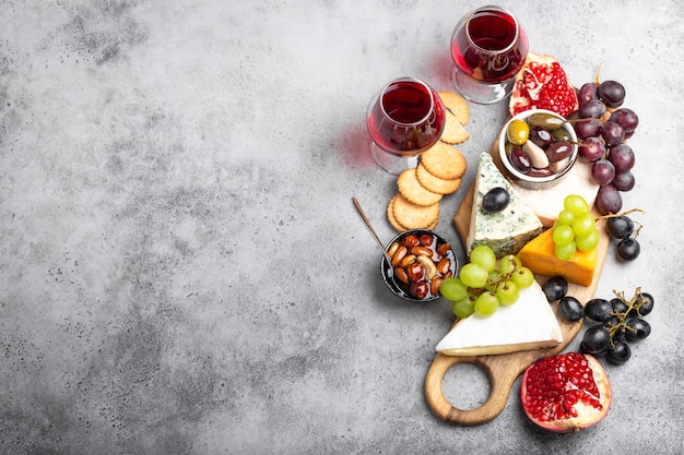 Selection of cheese and appetizers, wine in glasses, camembert, brie, cheddar, cracker, grapes, nuts, honey. Assorted mix of cheese on rustic wooden board with space for text, top view, close-up