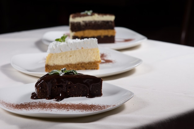 Selection of desserts at a restaurant with a diagonal line of three different varieties of cake served on plates with a slice or chocolate tart in the foreground