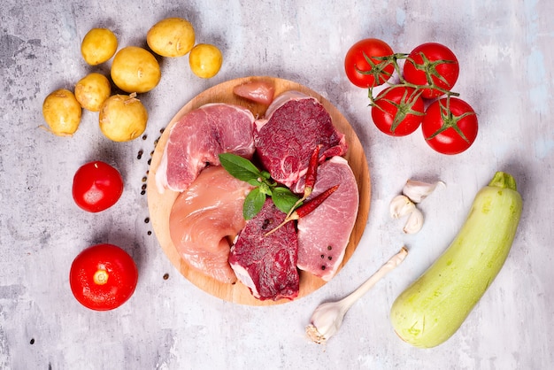 Selection of different raw meat with vegetables at wooden board .Lean proteins.