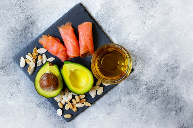 Selection of healthy fat sources, avocado, salmon, nuts, olive oil on a black plate. The concept of healthy eating. Top view, copy space, gray background