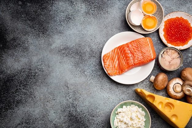 Selection of natural sources of vitamin D: fresh salmon, caviar, cheese, mushrooms, tuna, eggs on gray stone background top view. Foods and products rich in vitamin D. Template or space for text