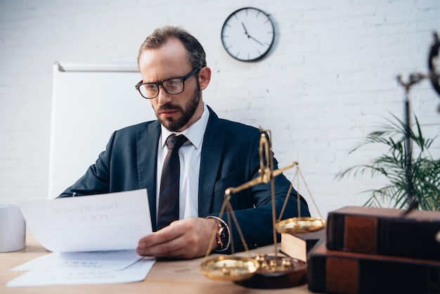 Selective focus of bearded lawyer looking at documents near golden scales and books