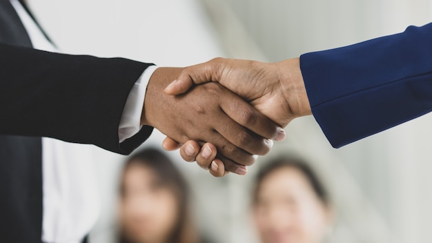 Selective focus on business women's hands in formal suits doing hand shake during business meeting with blurry colleagues in background. Concept for business meeting.