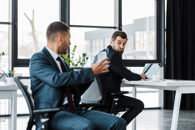 selective focus of businessman holding using laptop and sitting near colleague