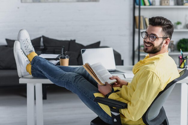 Photo selective focus of cheerful man studying with legs on table in modern office