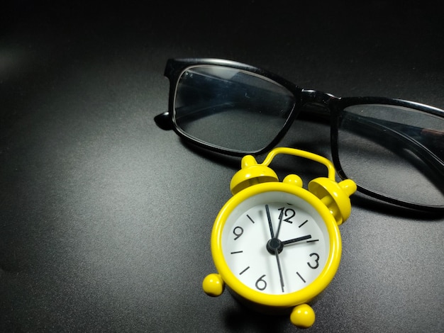 Selective focus of clock and glasses on black background with copy space