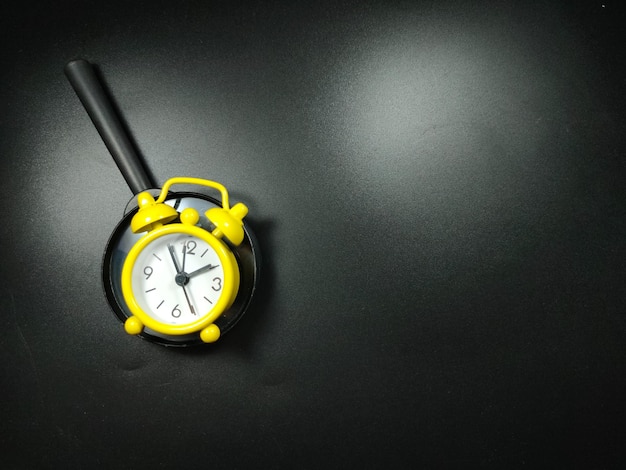 Selective focus of clock and magnifying glass on black background with copy space