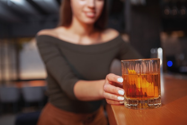 Selective focus on cocktail glass in the hand of a woman at the bar