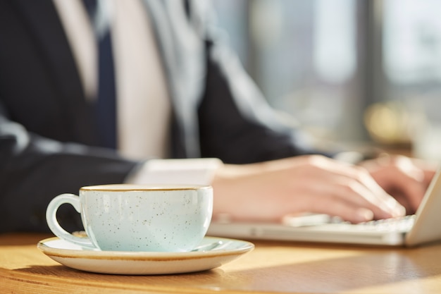 Selective focus on a coffee cup, business man working on laptop on background