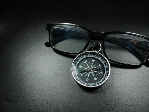 Selective focus of compass and glasses on black background with copy space