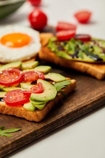 selective focus of cutting board with toasts scrambled egg cherry tomatoes and avocado on white