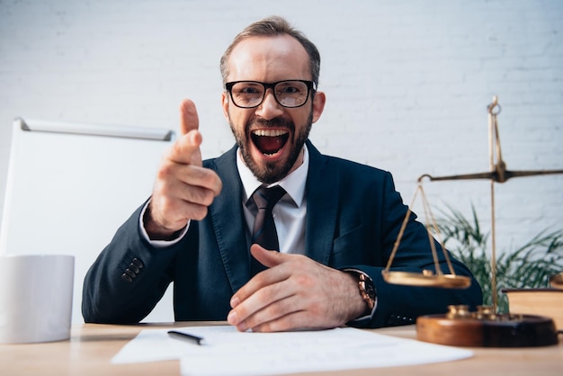 Photo selective focus of excited and bearded lawyer pointing with finger near scales