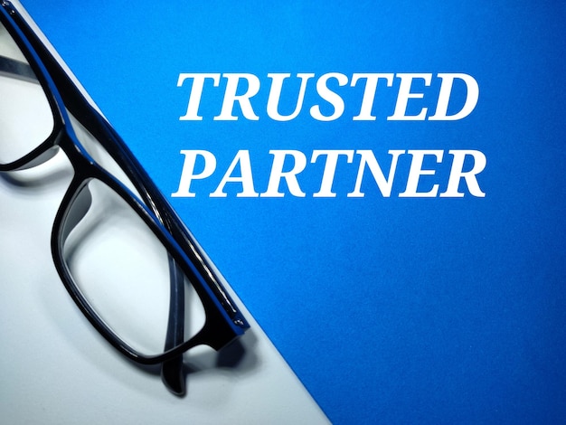 Selective focus of a eye glasses and text TRUSTED PARTNER on a white and blue background