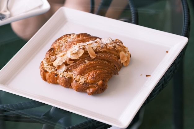 Selective focus Fresh croissant with almond slice on top on the white plate in the hotel breakfast bakery and pastry bar Traditional french sweet toast patisserie almond toast with cafe background