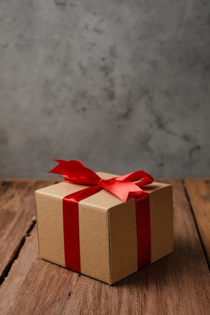 Selective focus of gift box with red ribbon and love shaped paper over rustic wooden table, top view flat lay.