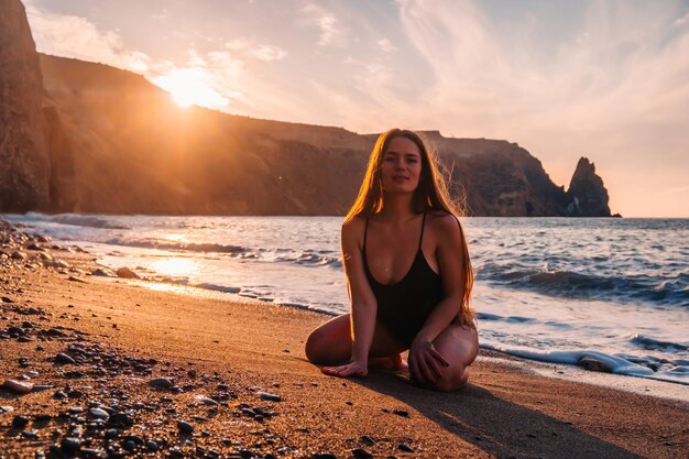 Selective focus happy carefree sensual woman with long hair in black swimwear posing at sunset beach