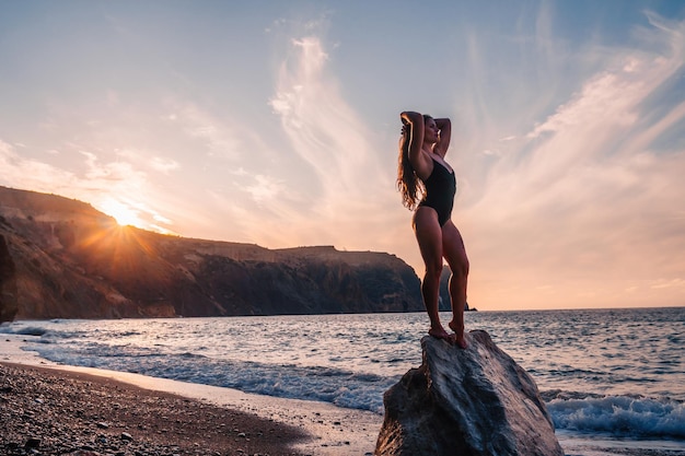 Selective focus happy carefree sensual woman with long hair in black swimwear posing at sunset beach