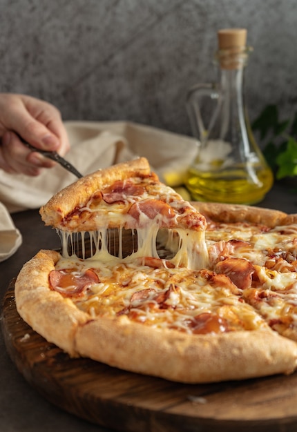 Selective focus. hot pizza with cheese and pepperoni. the girl pulls a slice of pizza with melted cheese stretching. vertical position, dark mood