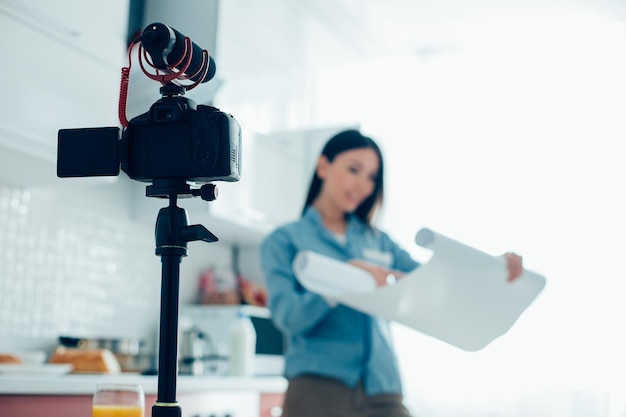 Selective focus of a modern camera on a tripod Woman with a paper roll standing on the background