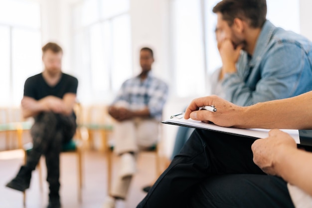 Photo selective focus of multi ethnic support group during meeting with professional mature male therapist group of men and women looking serious