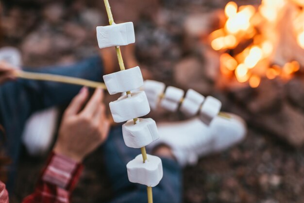 Photo selective focus of puffy marshmallows on sticks near couple and bonfire